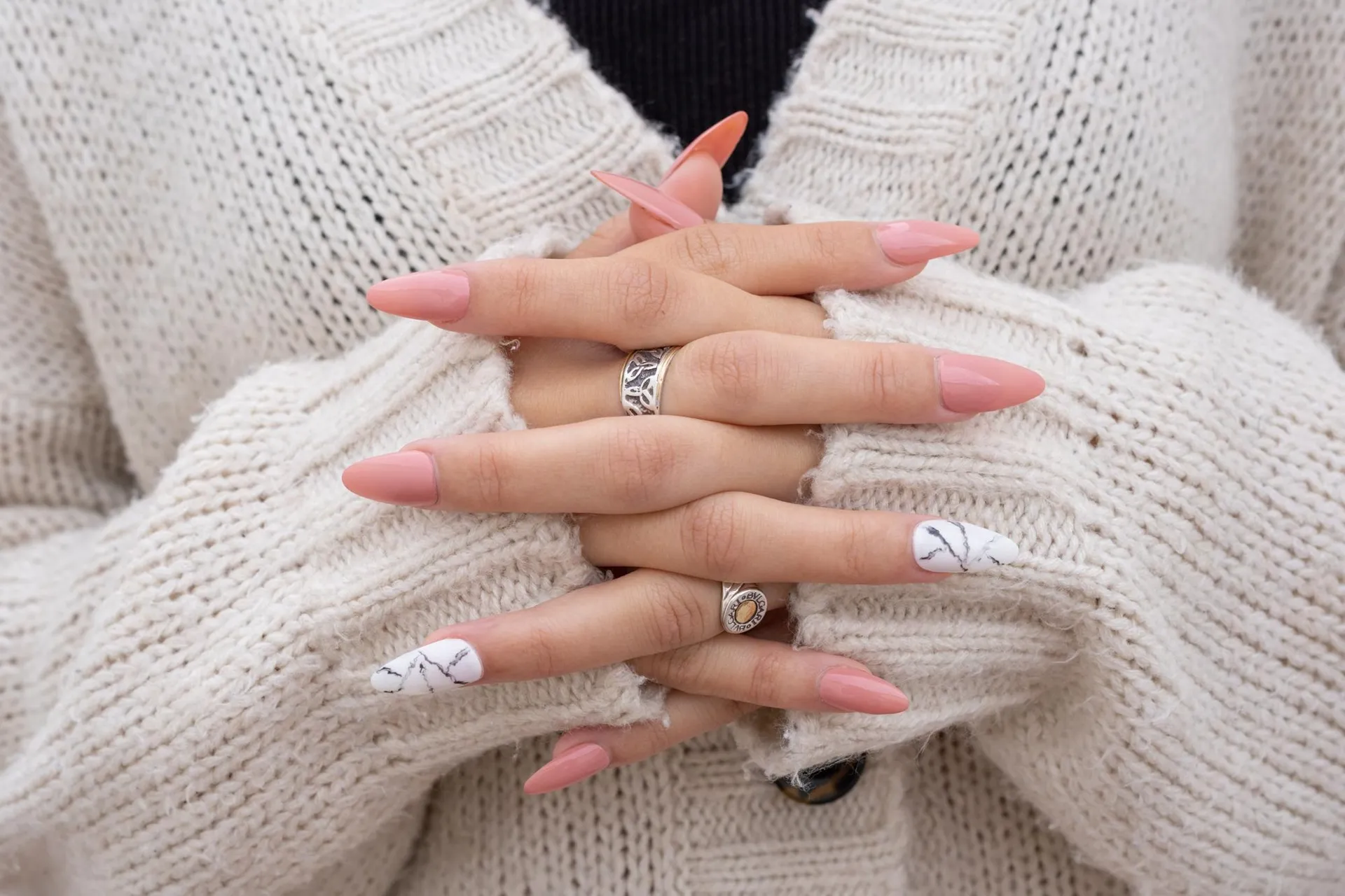 woman's hands with crossed fingers pink sculpted fingernails rings